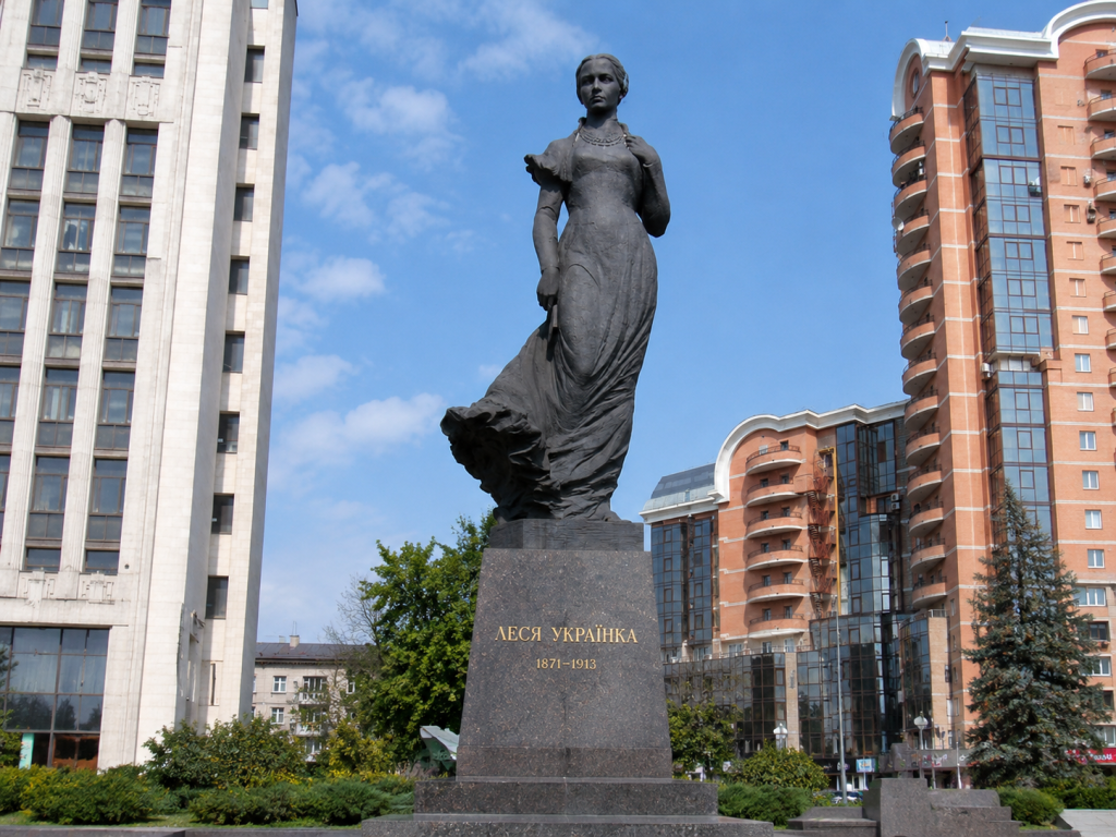 Пам'ятник Лесі Українці у Києві на тлі сучасної міської забудови в ясний сонячний день.